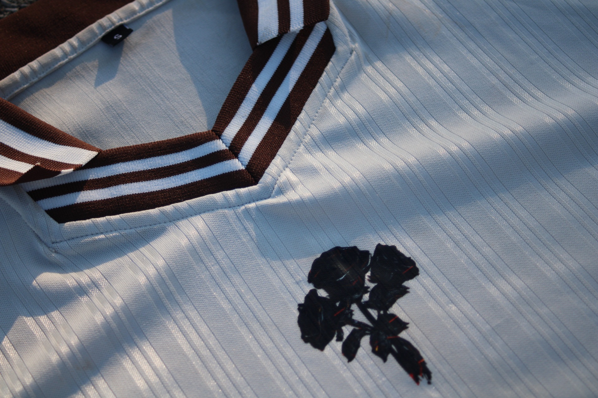 Close detail of the striped knit V-neck collar and black embroidered floral icon on satin pinstripe fabric